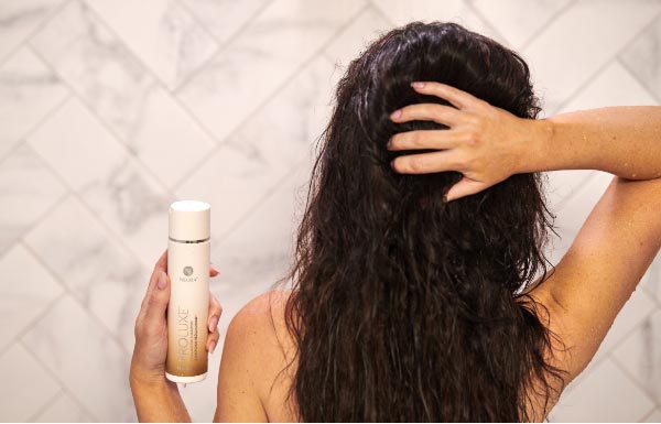 Image of woman's hair while she holds a bottle of ProLuxe Shampoo.